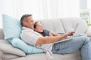 Father with daughter relaxing on the couch using laptop —  Heating in Hemet,CA