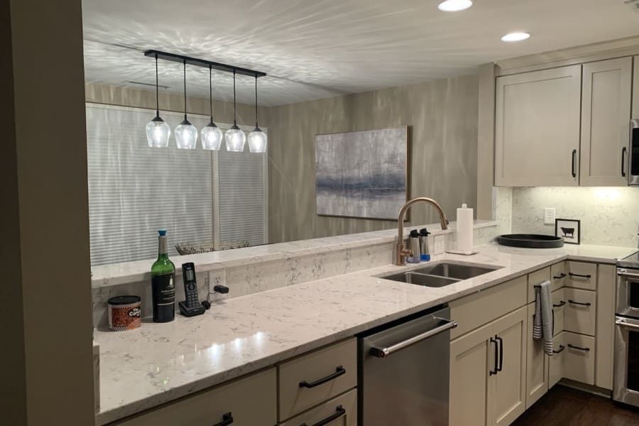 A kitchen with white cabinets , stainless steel appliances , a sink , and a large mirror.