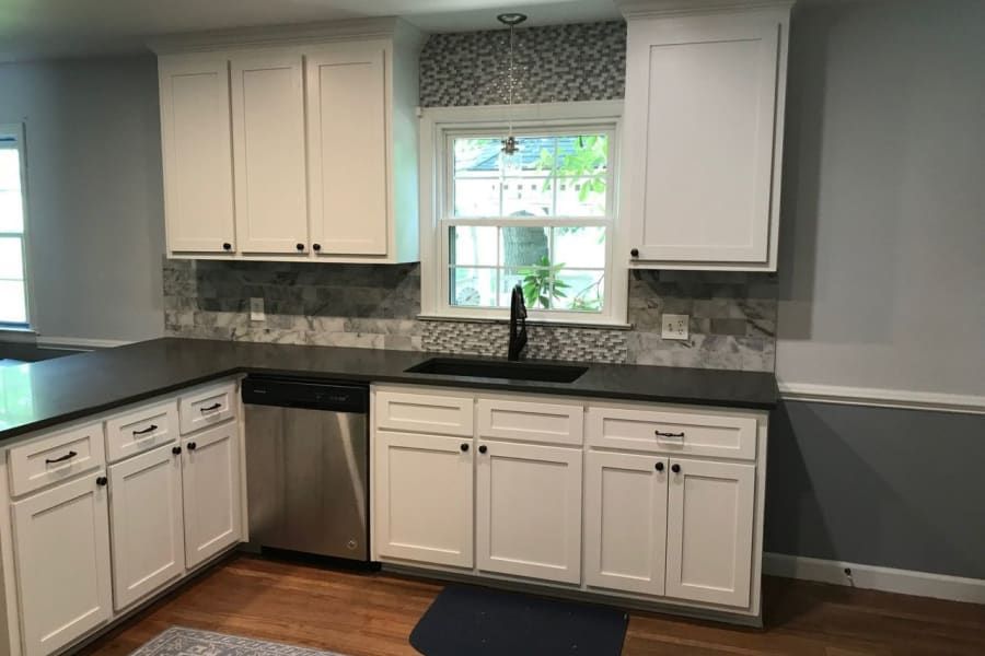 A kitchen with white cabinets , stainless steel appliances , a sink and a window.