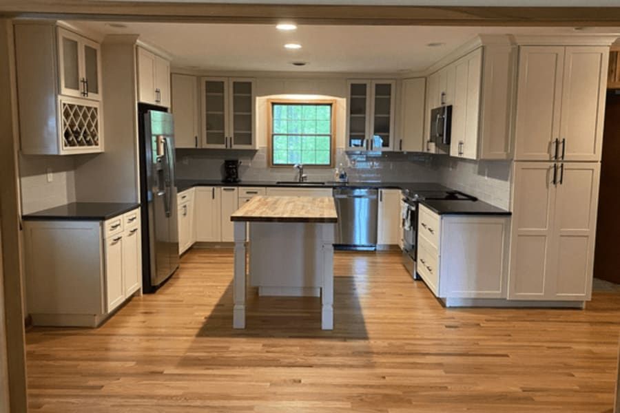 A kitchen with white cabinets , stainless steel appliances , hardwood floors and a large island.