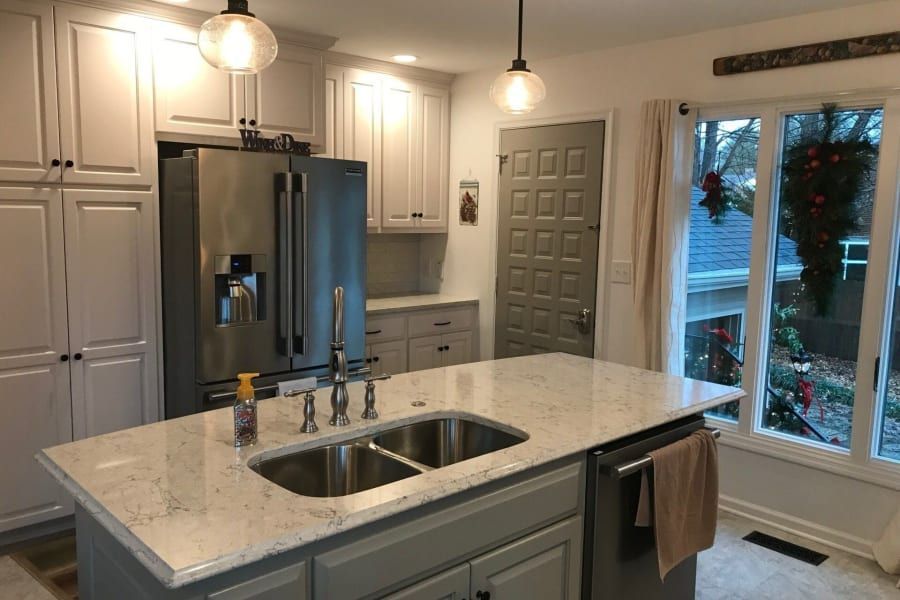 A kitchen with white cabinets , stainless steel appliances , a sink and a refrigerator.