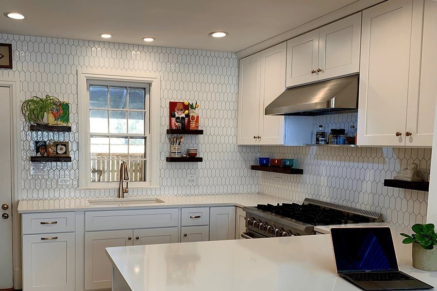 A kitchen with white cabinets , a stove , a sink , and a laptop on the counter.