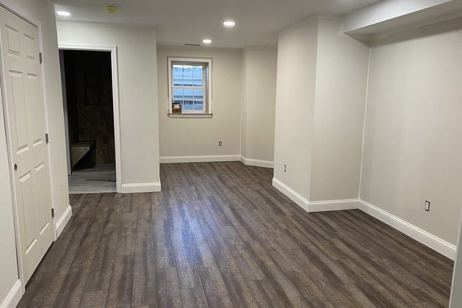 An empty basement with hardwood floors and white walls.