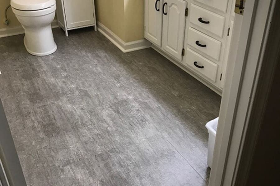 A bathroom with a toilet , sink , cabinets and a trash can.