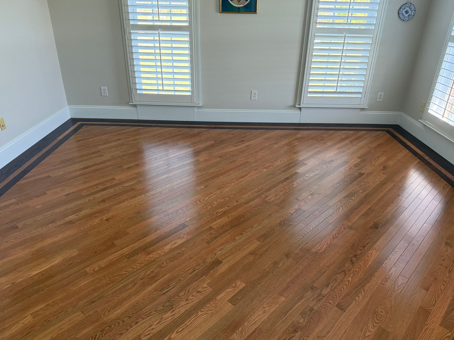 Empty room with wood flooring, gray walls, and windows with white blinds.