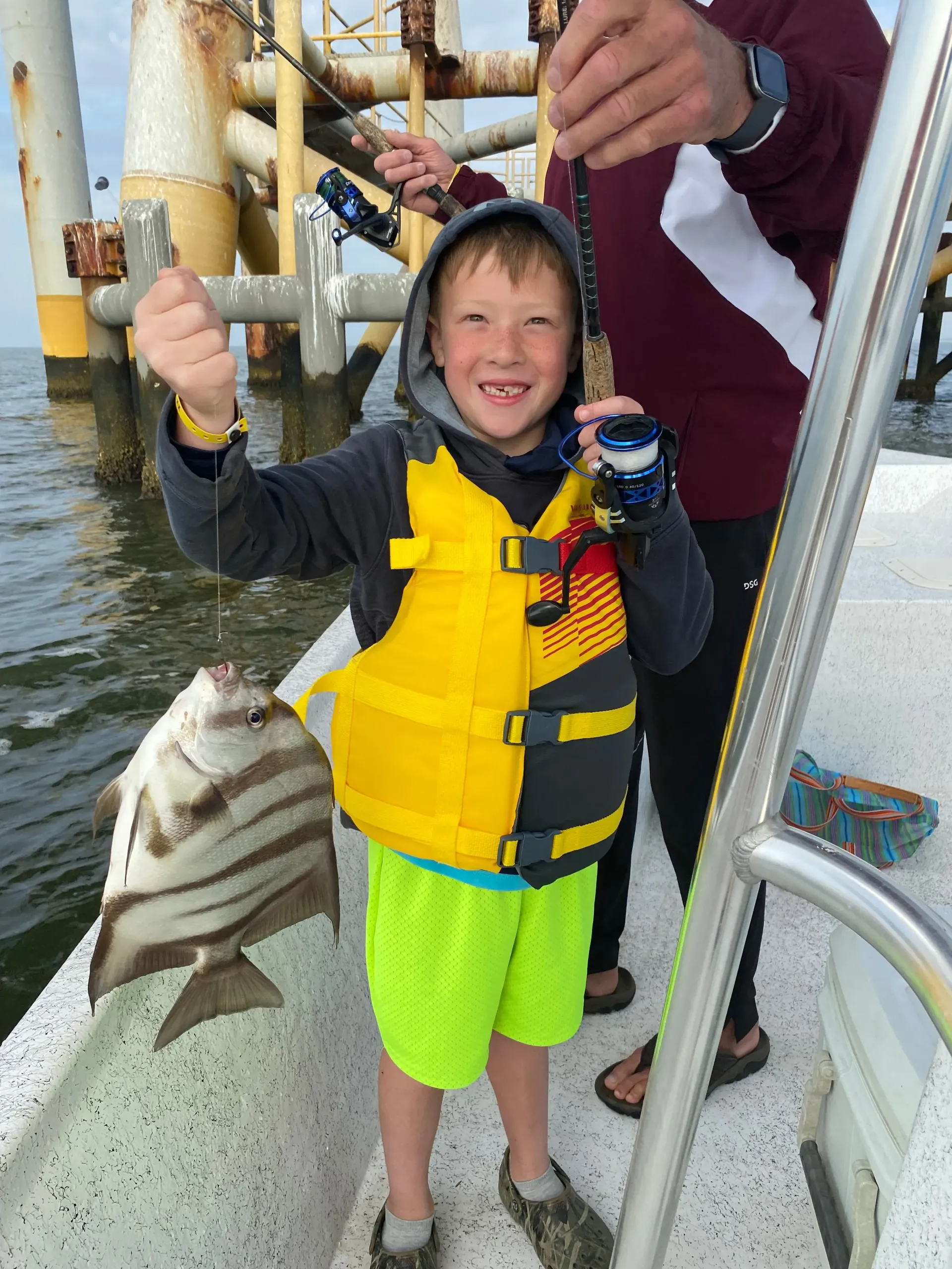 A young boy in a life jacket is holding a fish on a boat.