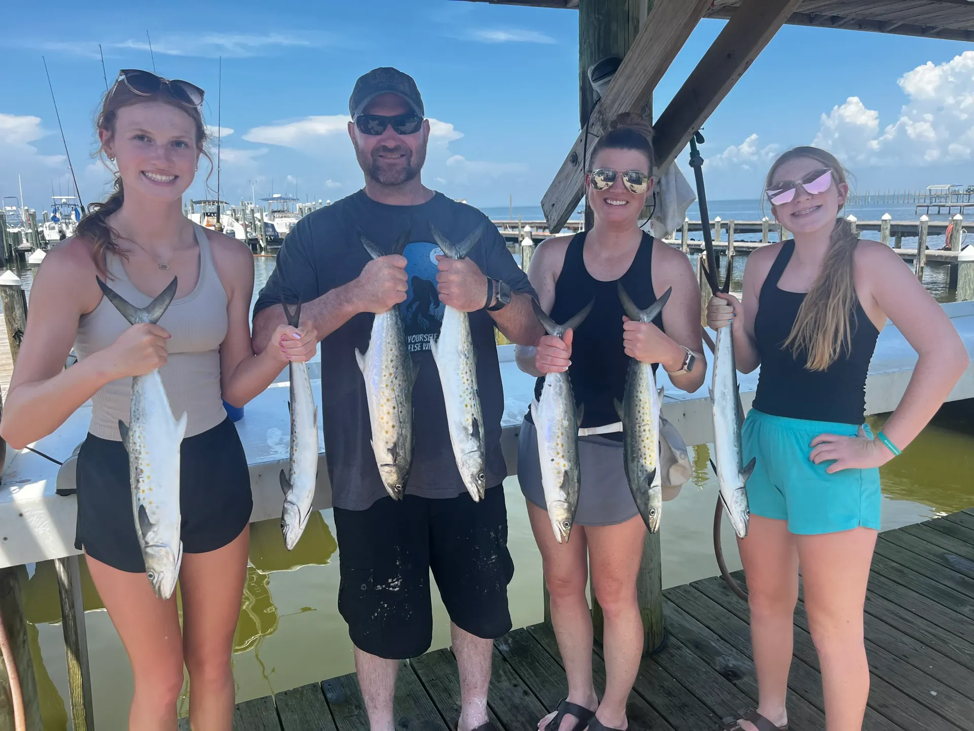 A group of people are standing on a dock holding fish.