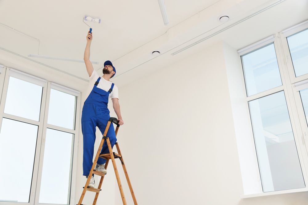 A man is standing on a ladder painting the ceiling.
