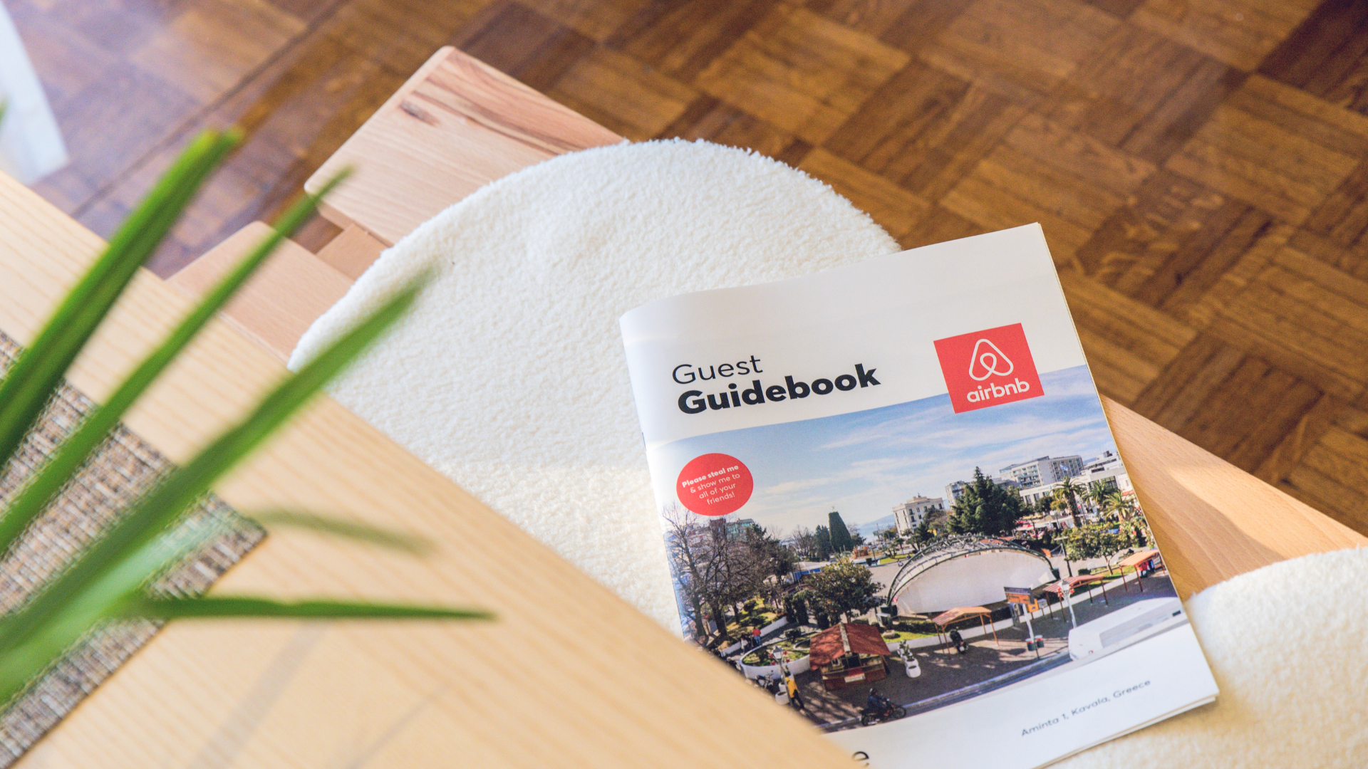 A guidebook is sitting on a wooden table next to a plant.