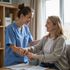 Nurse in blue scrubs assists a woman, both smiling, in a home setting.
