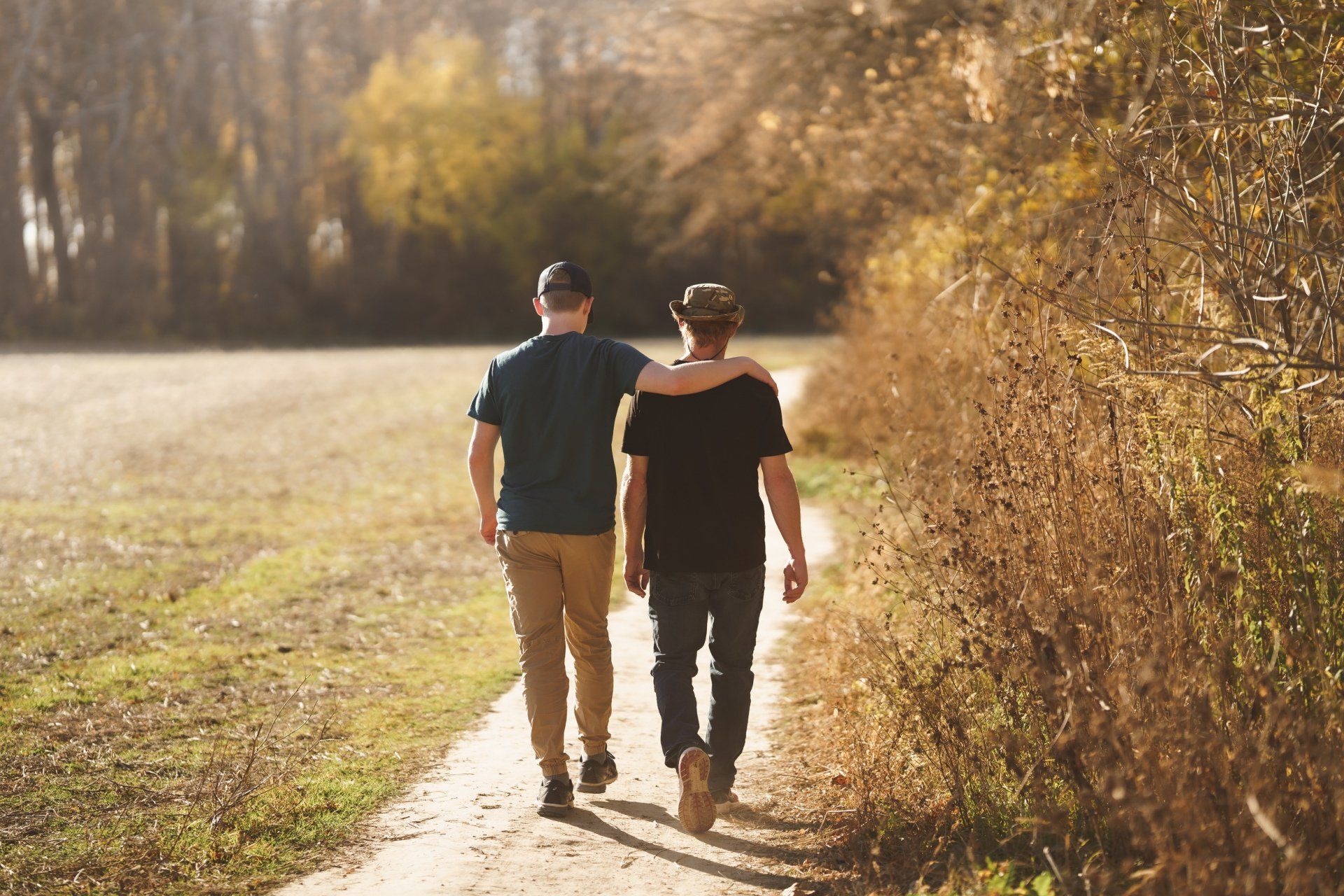 Two men are walking down a path with their arms around each other.