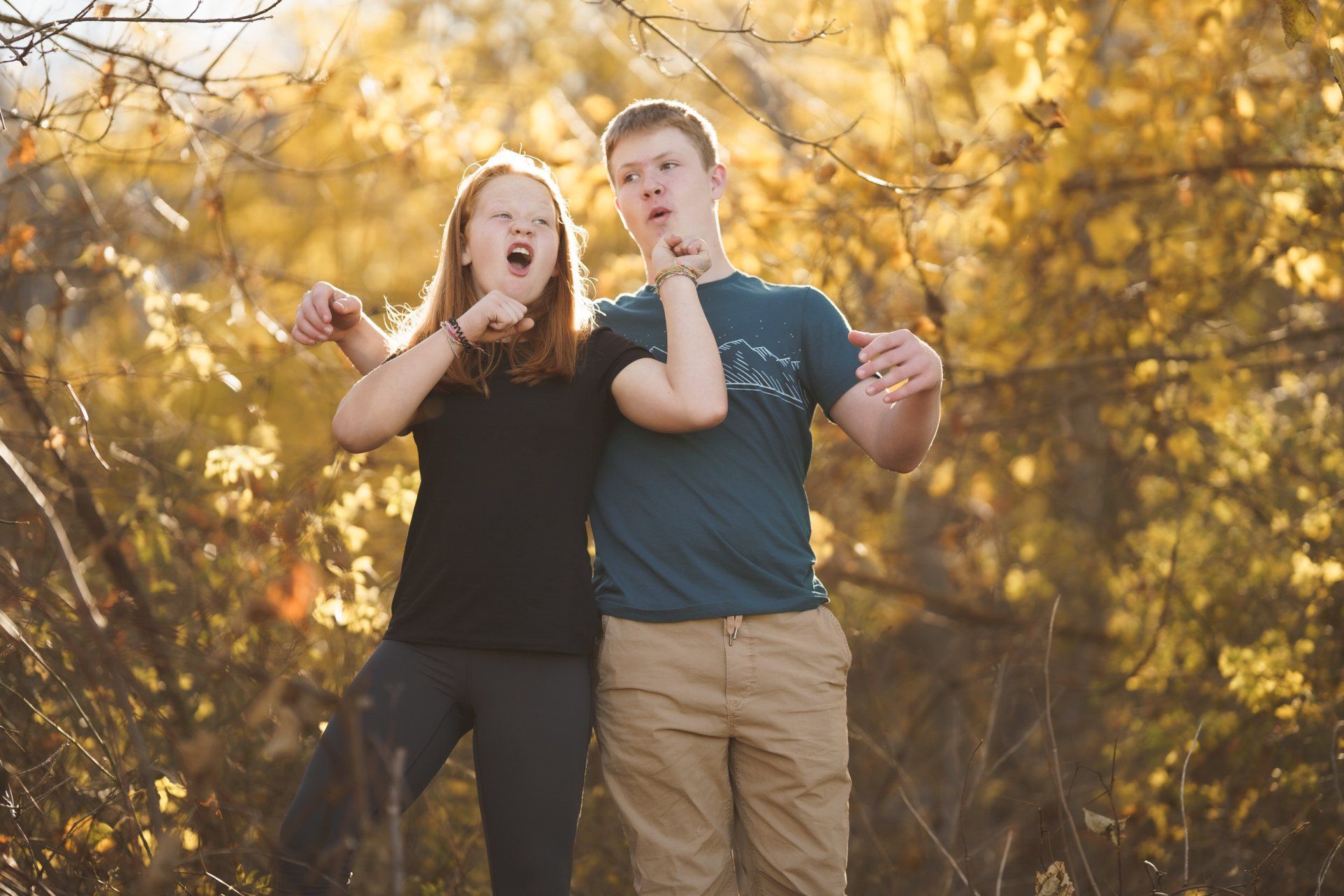 A boy and a girl are standing next to each other in the woods.