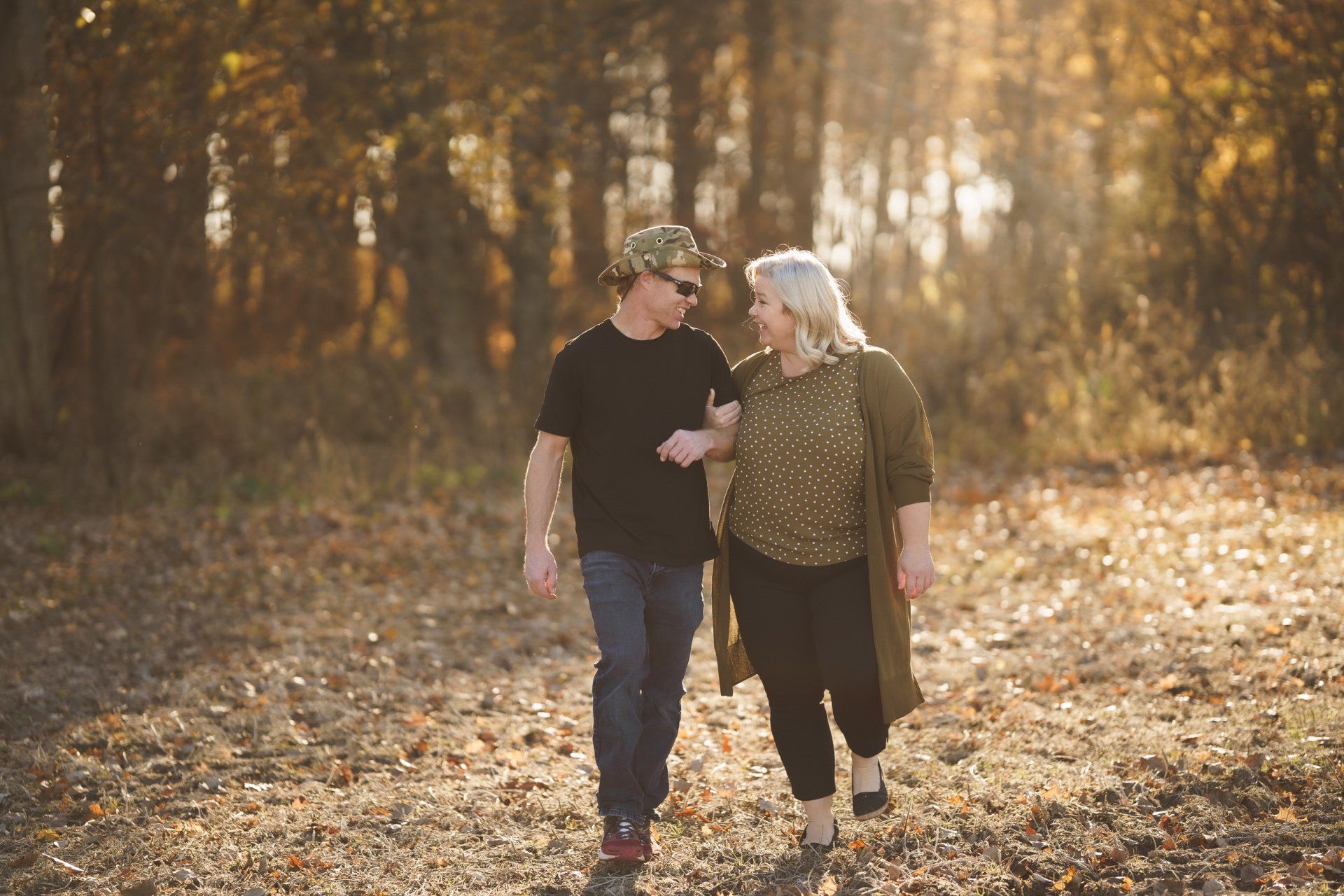 A man and a woman are walking through a forest holding hands.