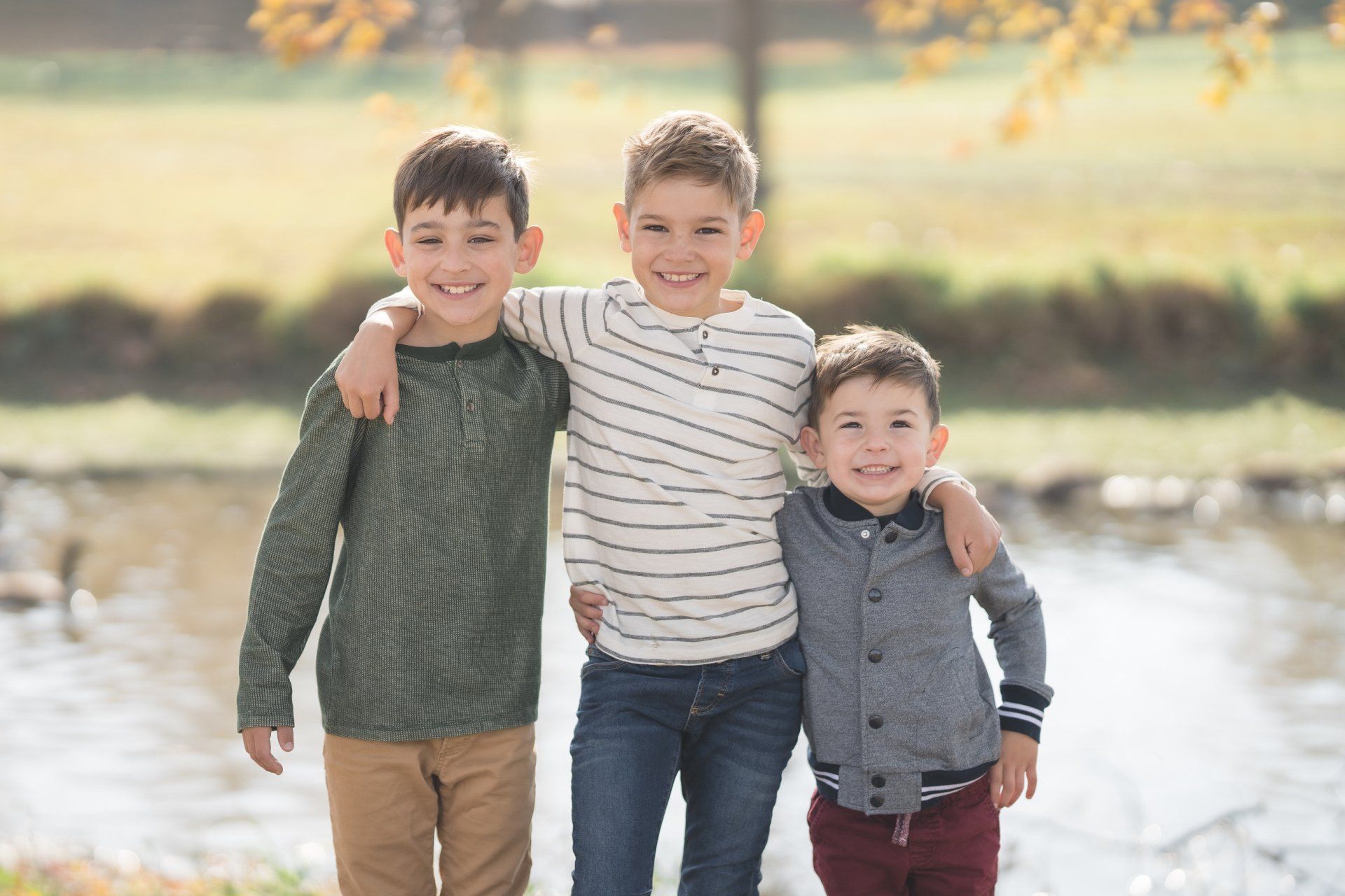 Three young boys are standing next to each other in front of a river.