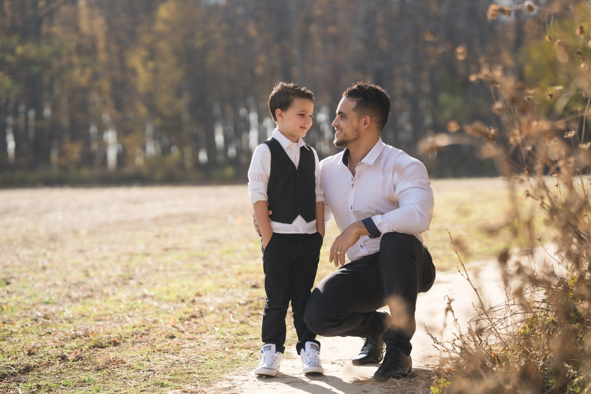 A man and a boy are kneeling down in a field and looking at each other.