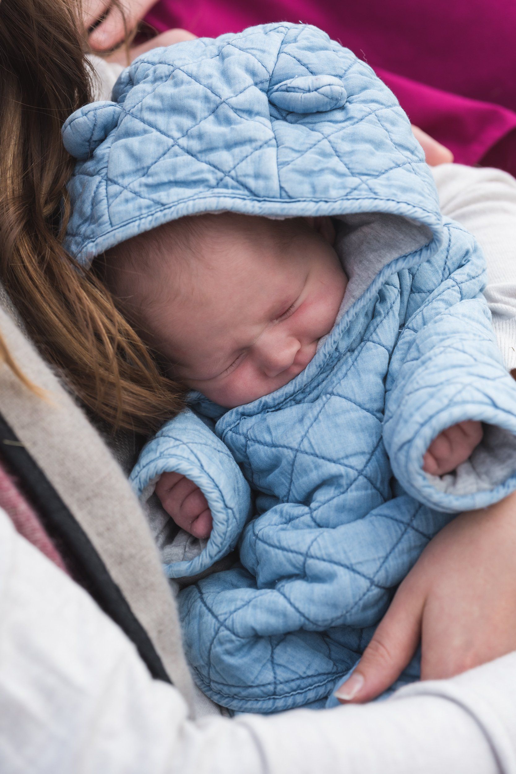 A woman is holding a baby in a blue blanket with a hood.