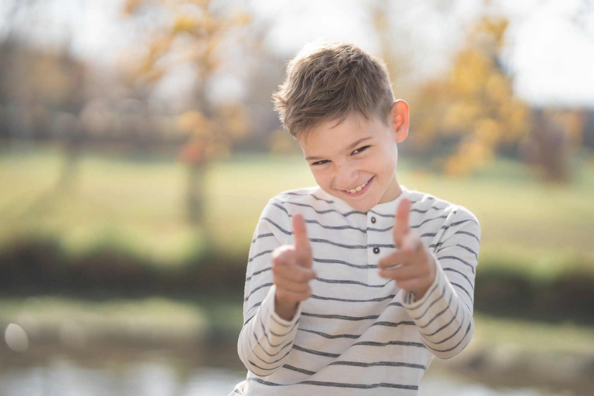 A young boy in a striped shirt is giving two thumbs up.