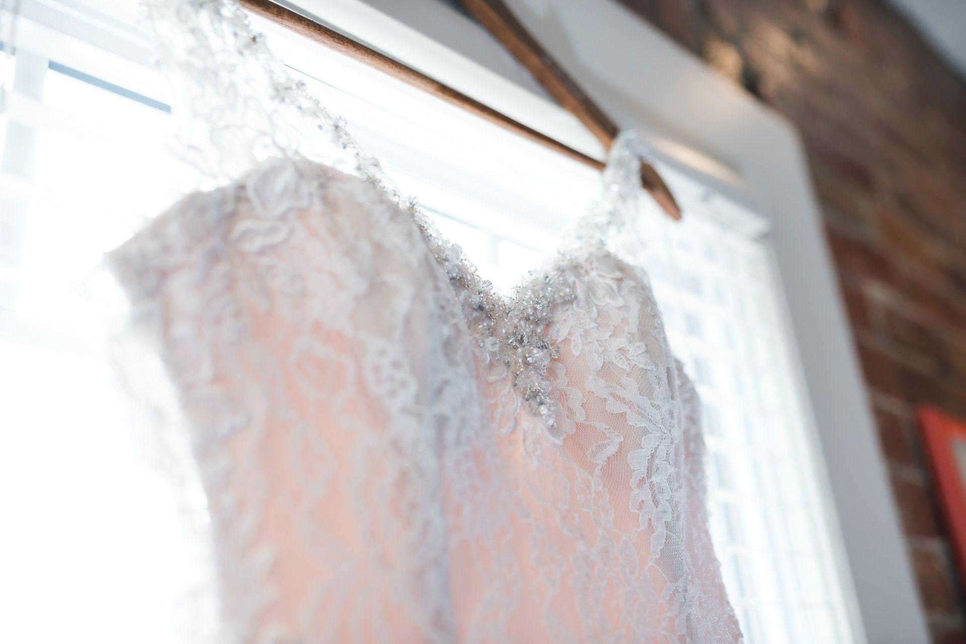 A wedding dress is hanging on a hanger in front of a window.