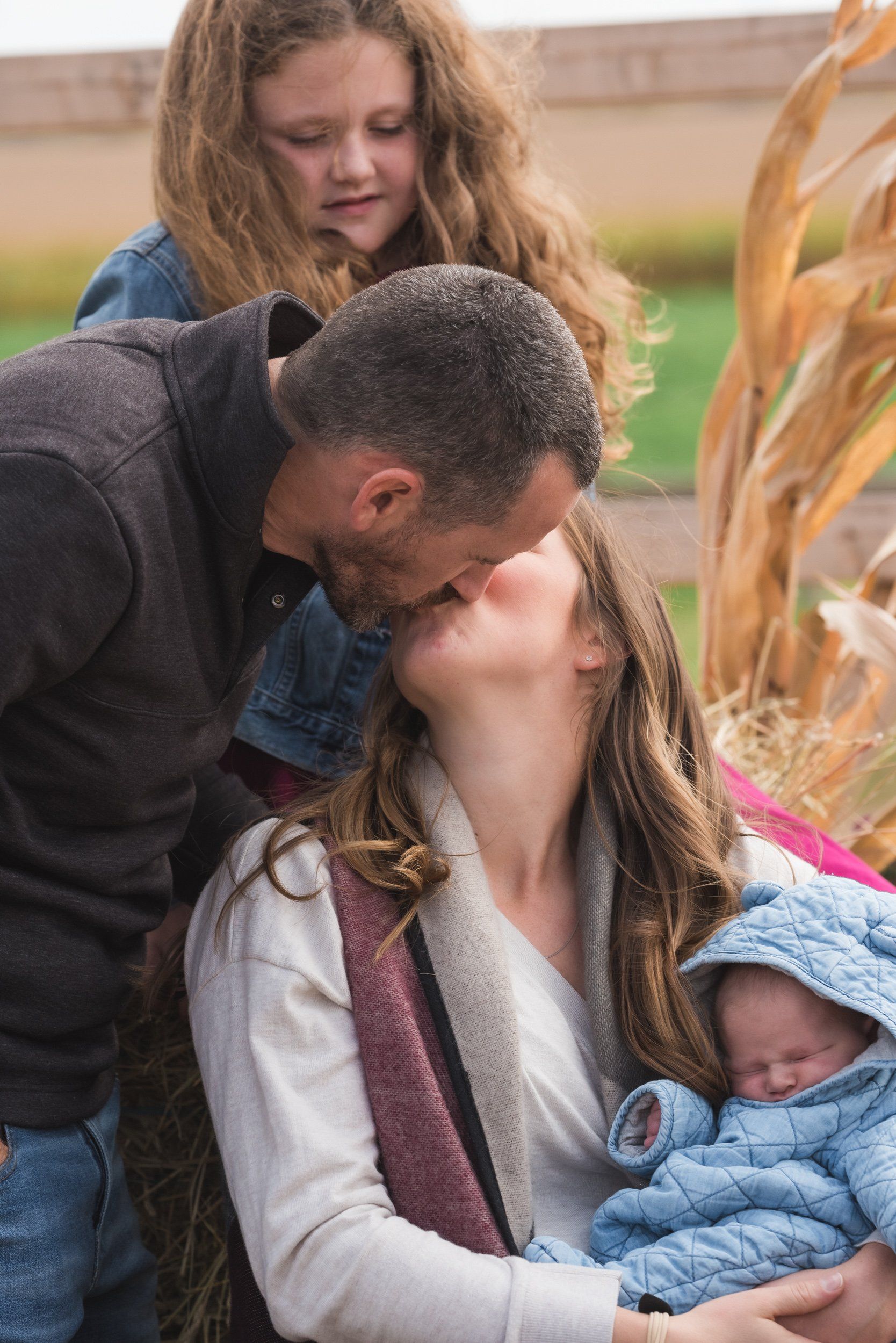 A man is kissing a woman on the cheek while holding a baby.