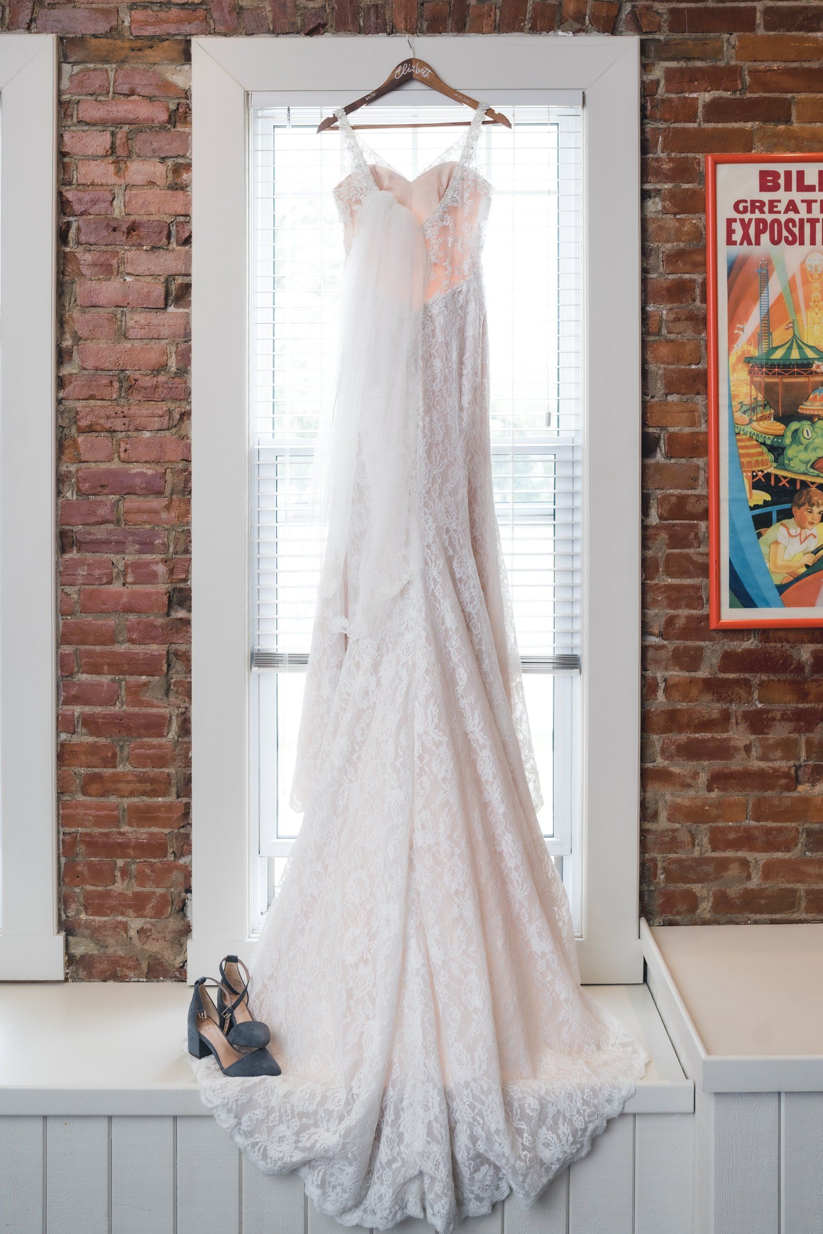A wedding dress is hanging on a hanger in front of a window.