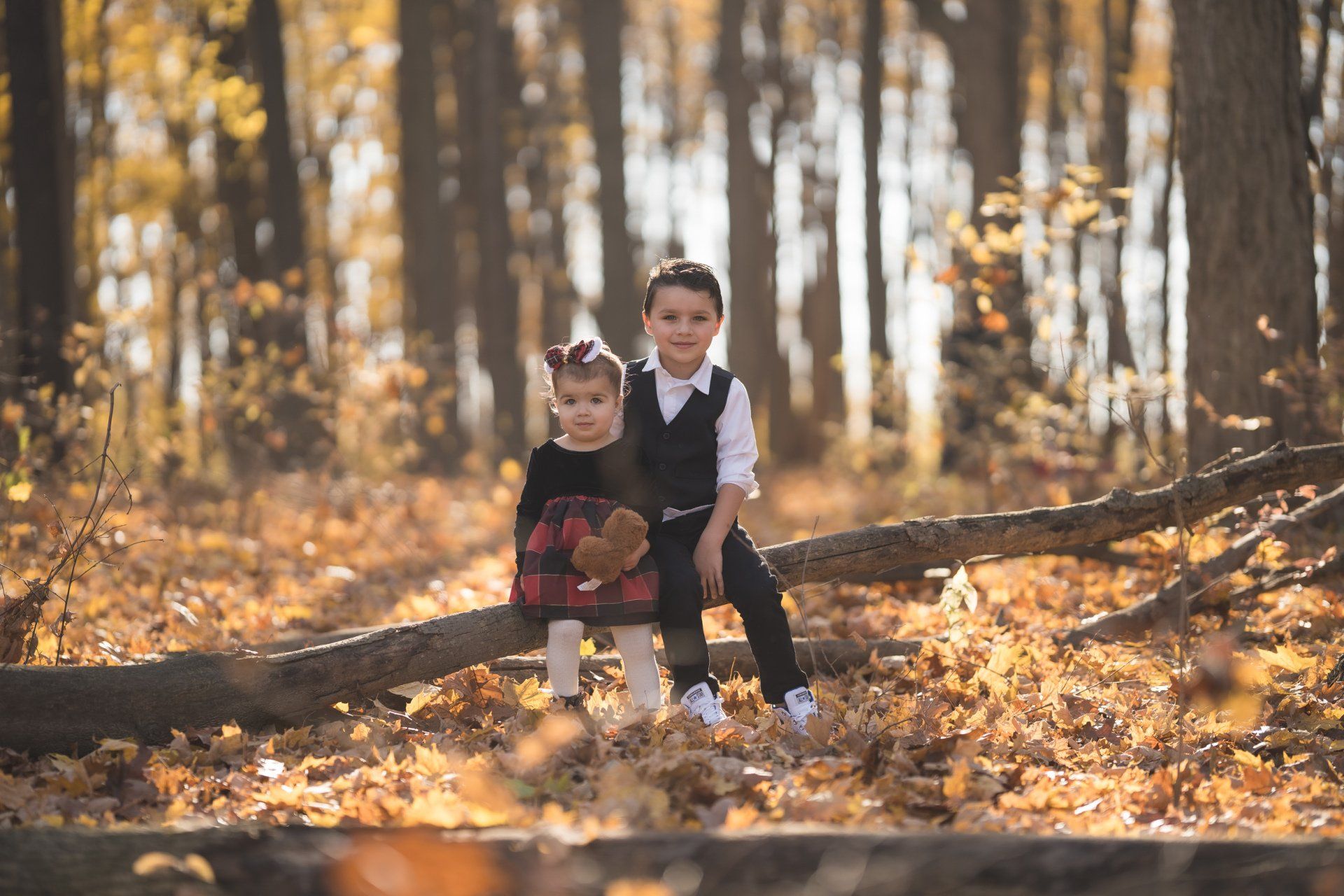 A boy and a girl are sitting on a log in the woods.