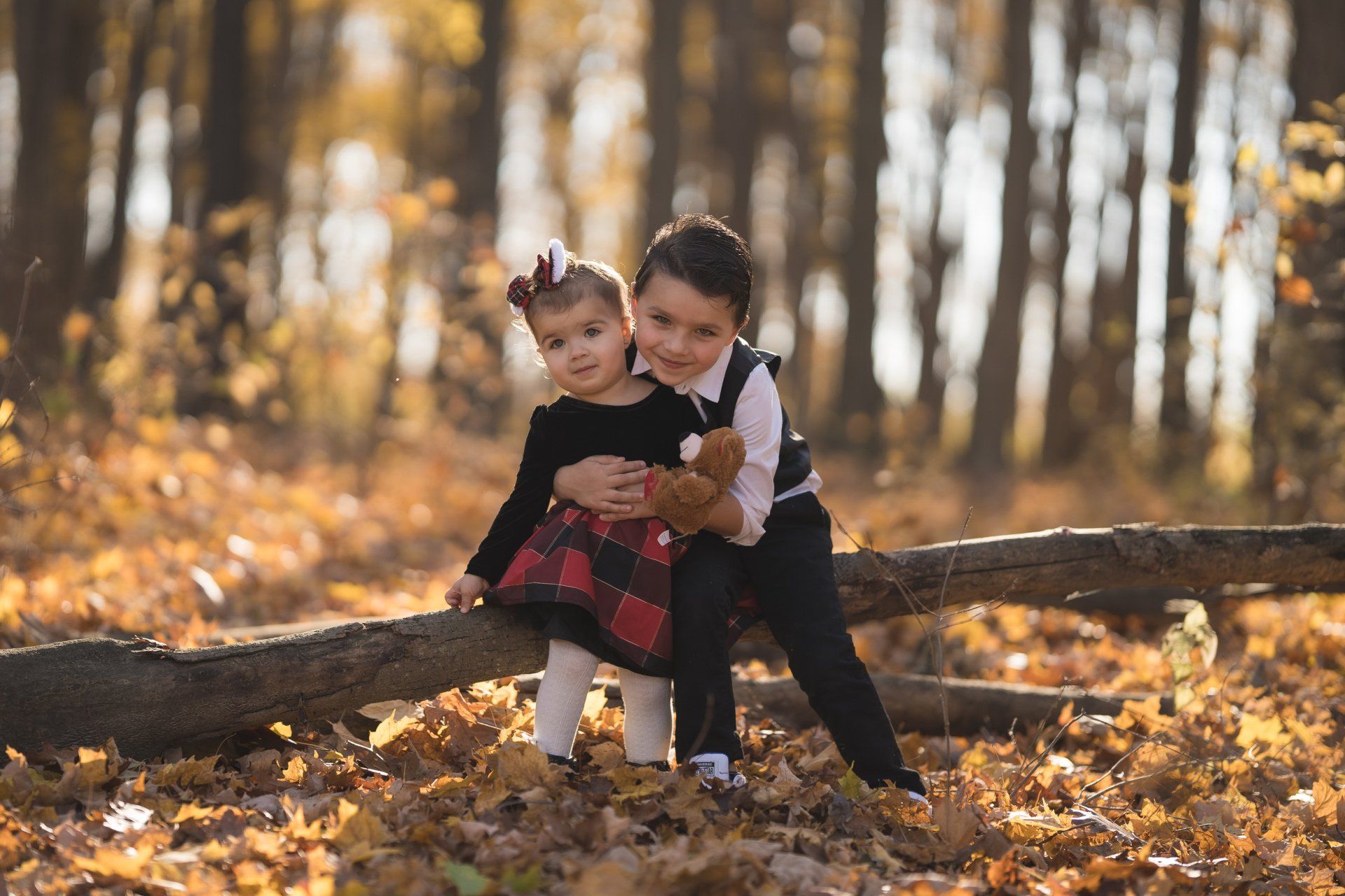 A boy and a girl are sitting on a log in the woods.