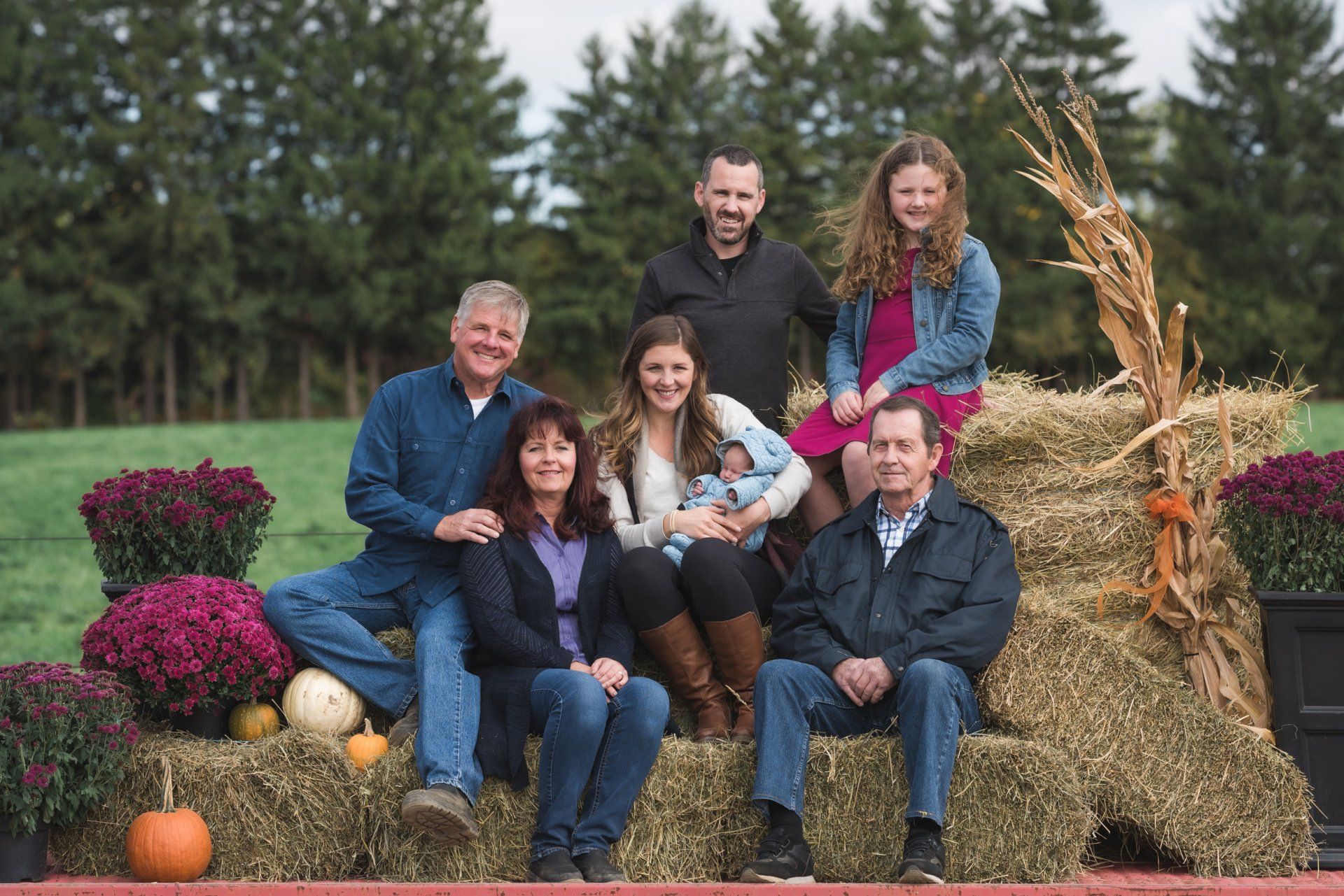 A family is posing for a picture while sitting on hay bales.