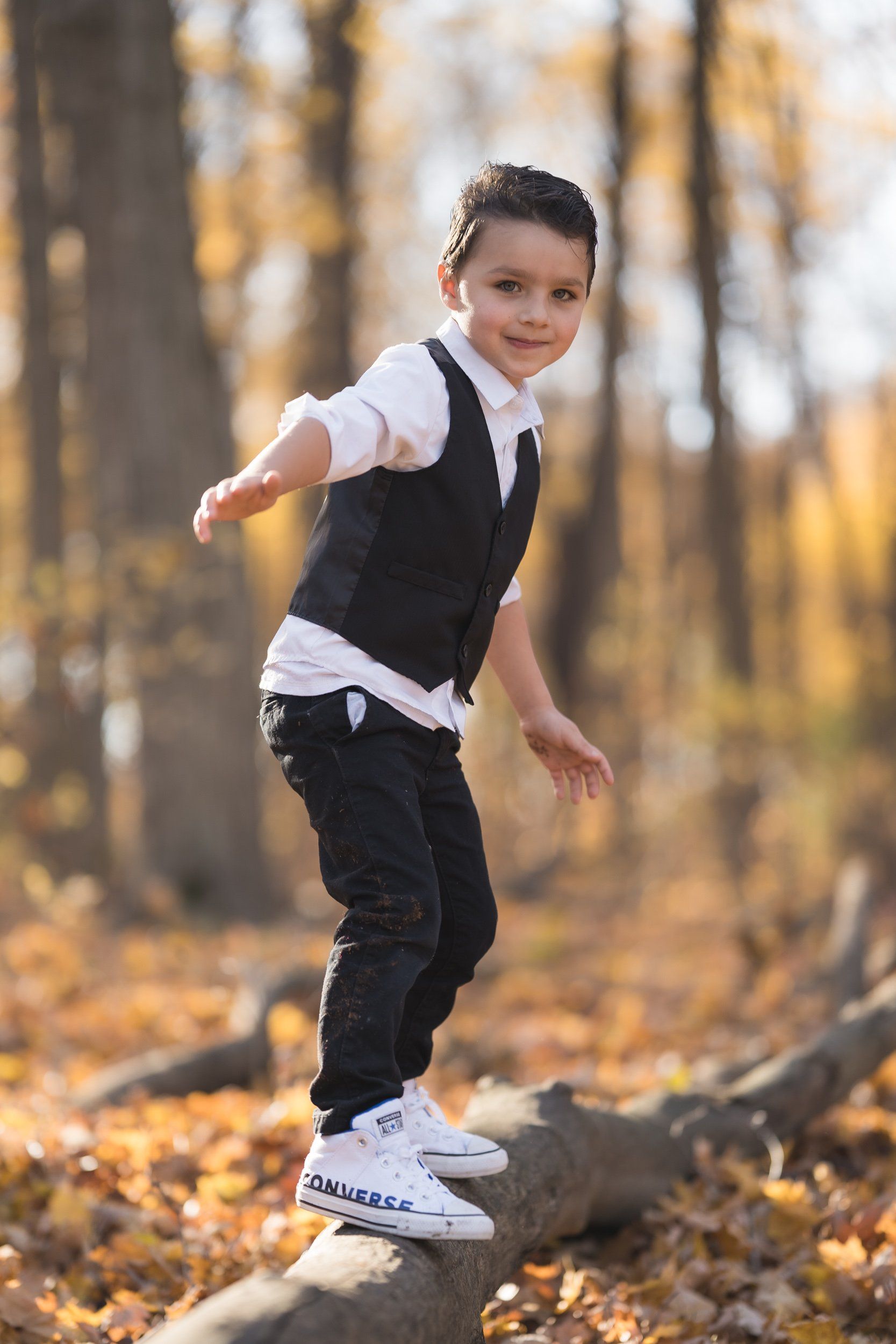 A young boy is standing on a log in the woods.