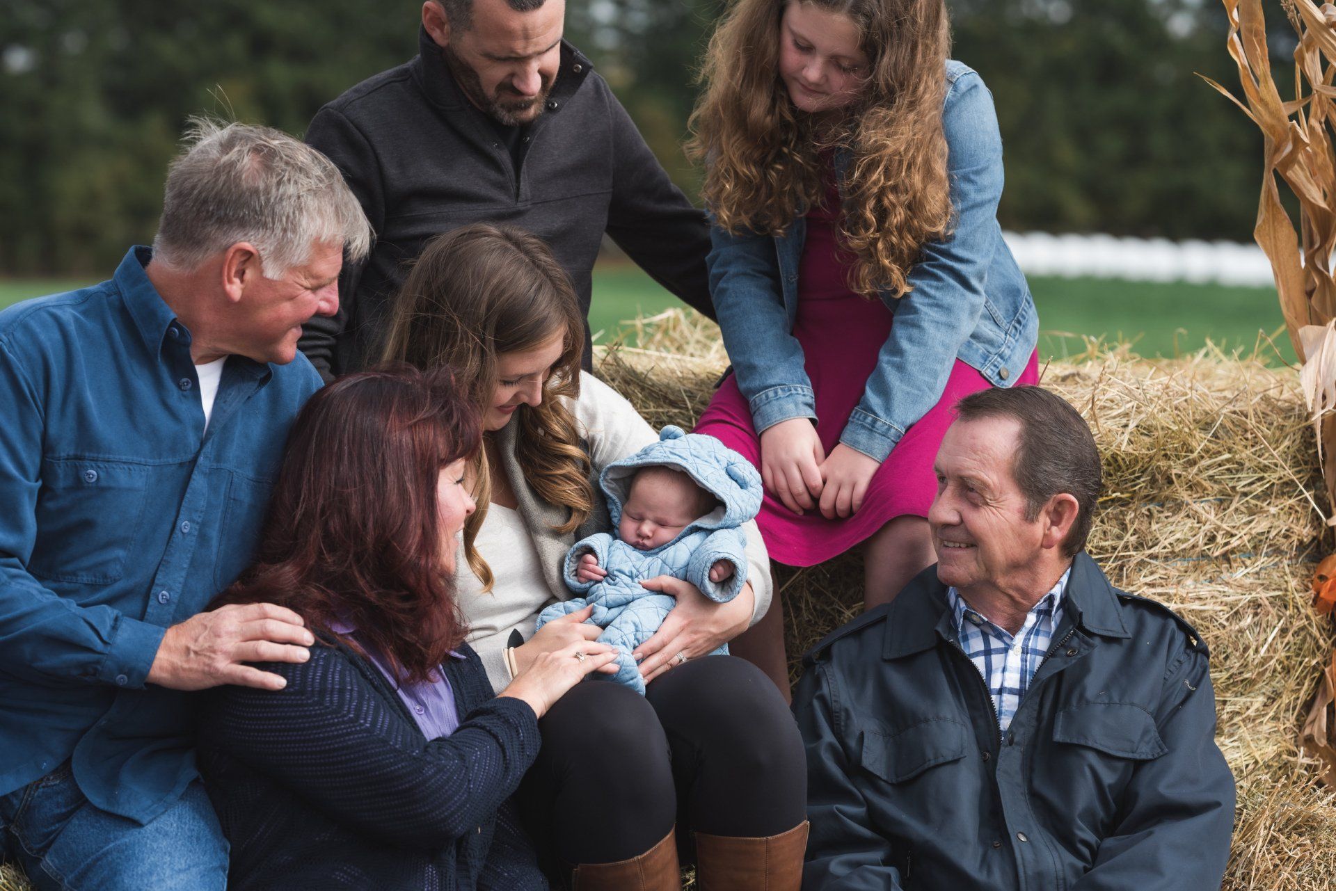 A family is sitting on a hay bale holding a baby.