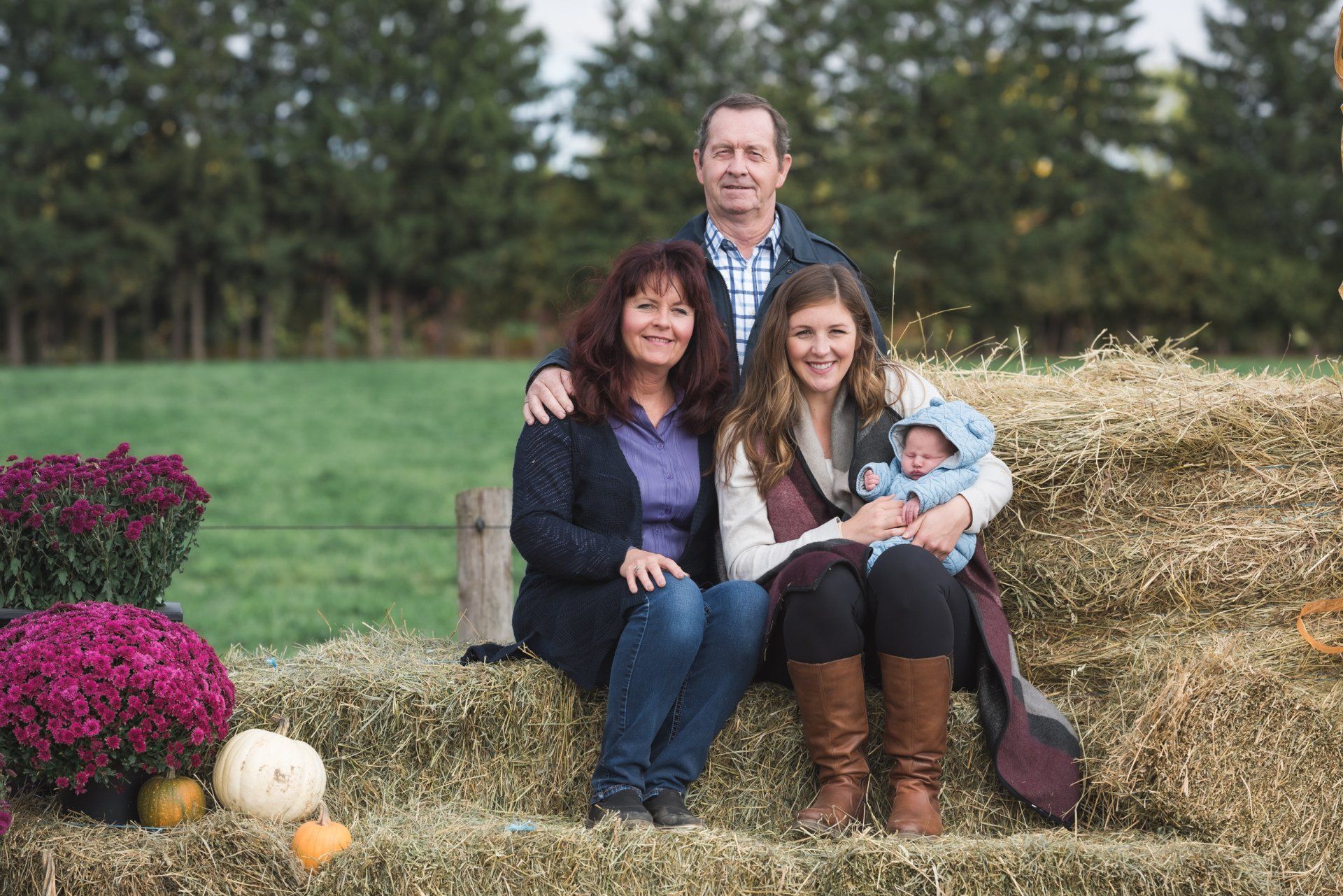 A family is posing for a picture while sitting on a bale of hay.