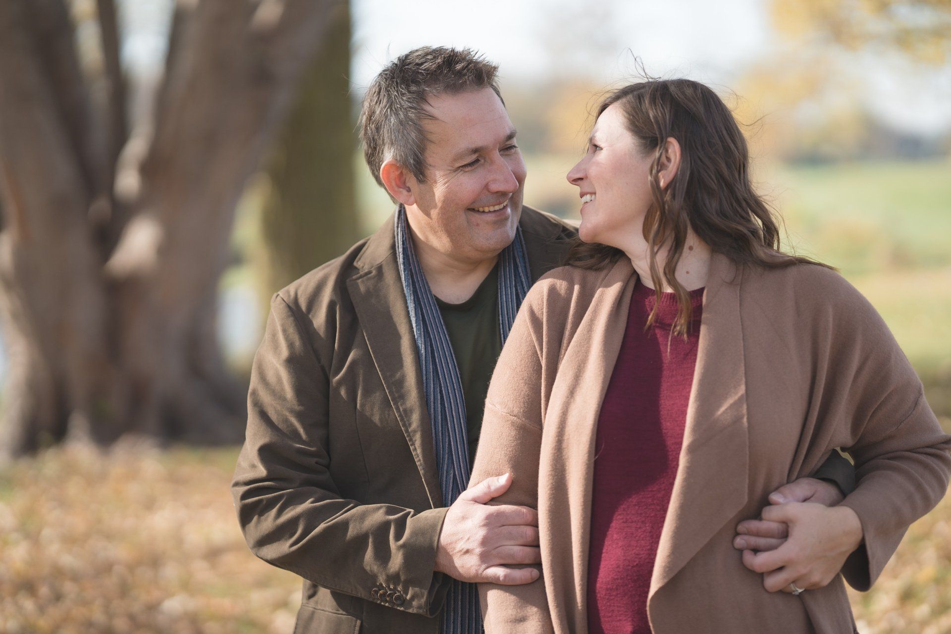A man and a pregnant woman are standing next to each other in a park.