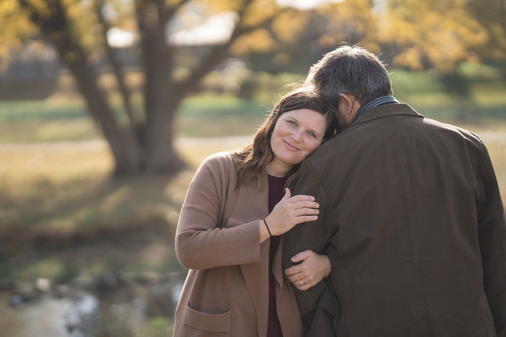 A man and a woman are hugging each other in a park.