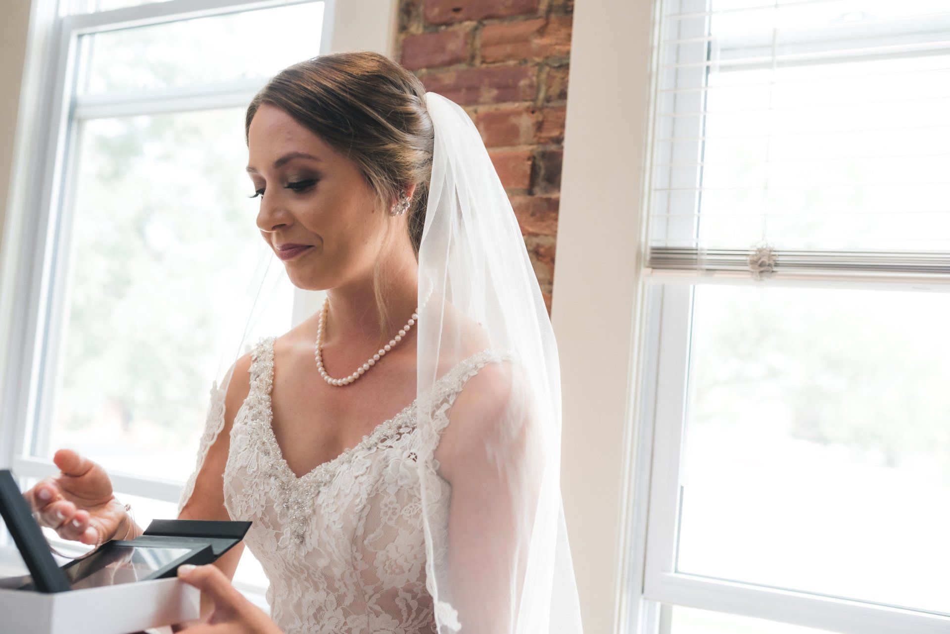 A bride in a wedding dress and veil is opening a gift box.