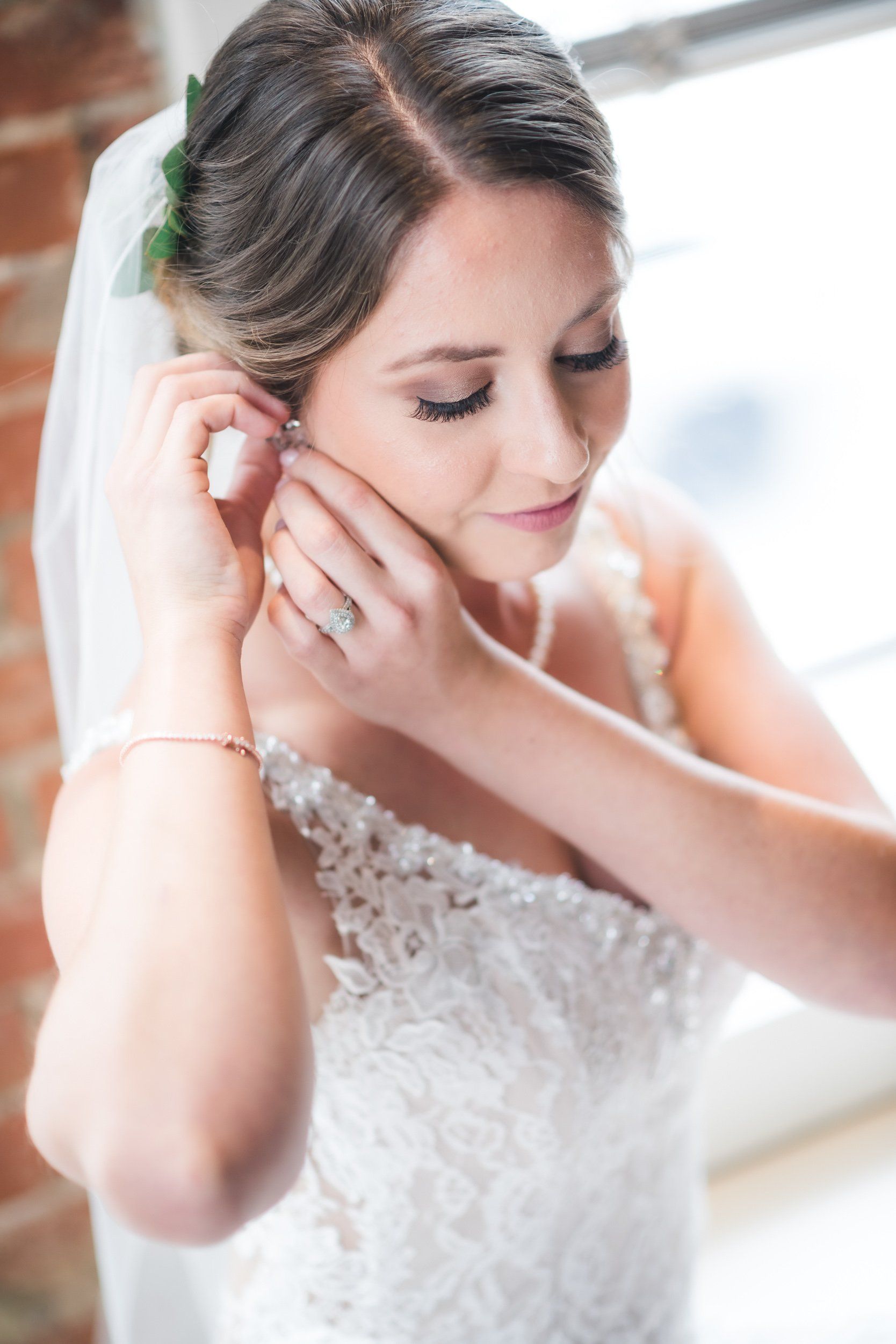 A bride is putting on her earrings in front of a window.