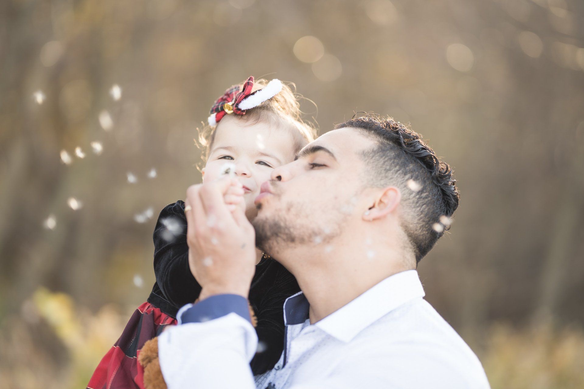 A man is kissing a baby girl on the cheek in a field.