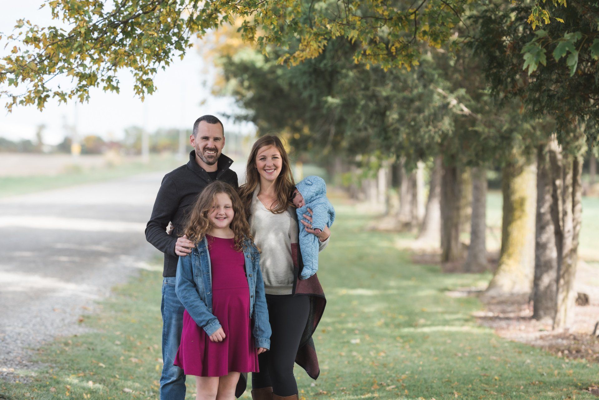 A family is posing for a picture in front of a row of trees.