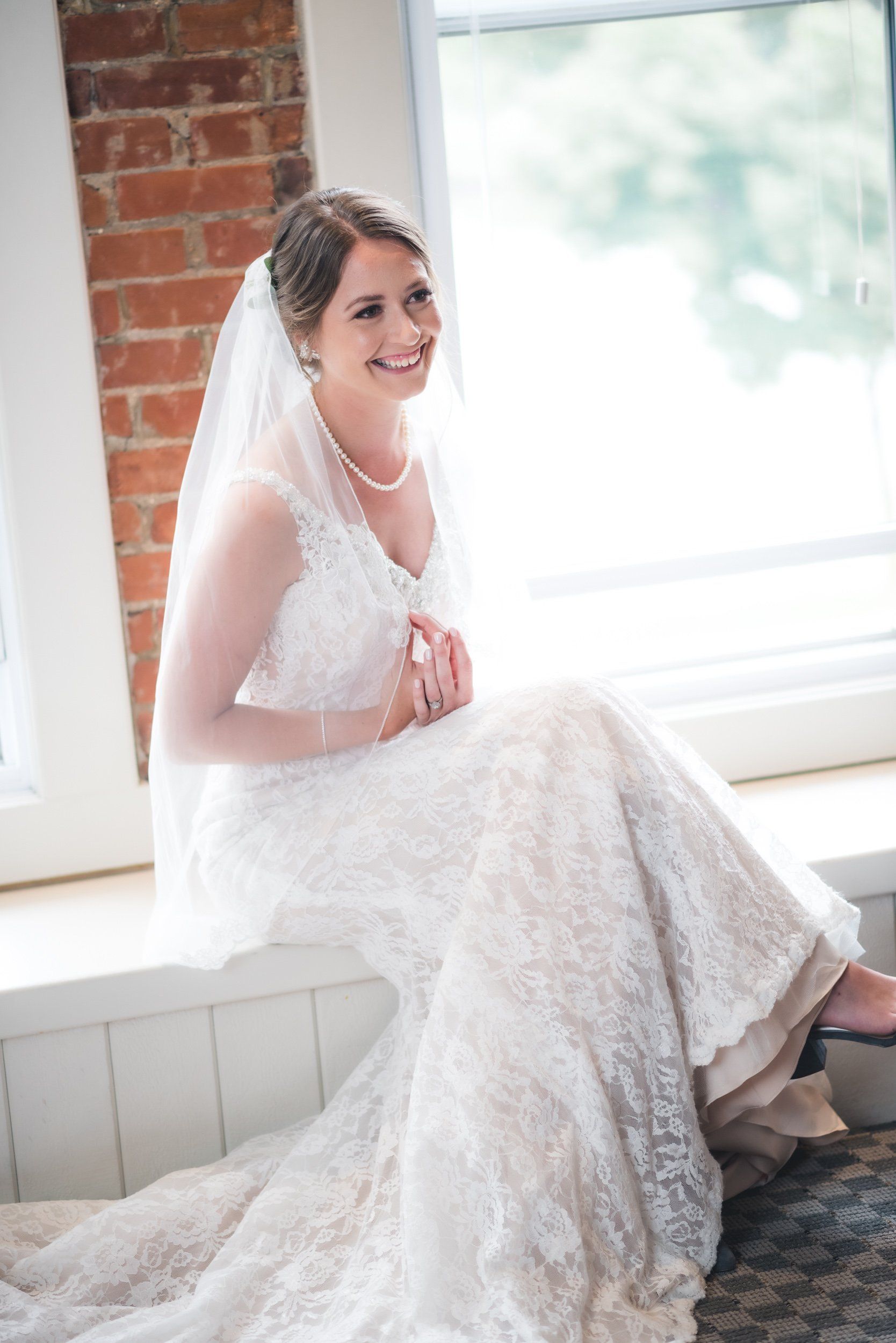 A bride in a wedding dress is sitting on a window sill.
