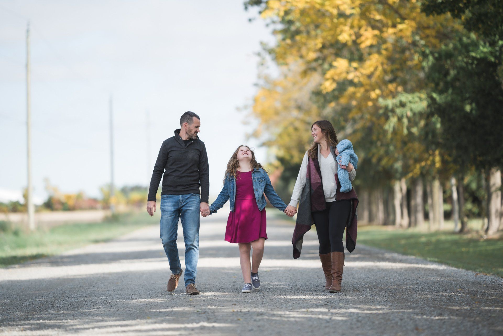 A family is walking down a road holding hands.