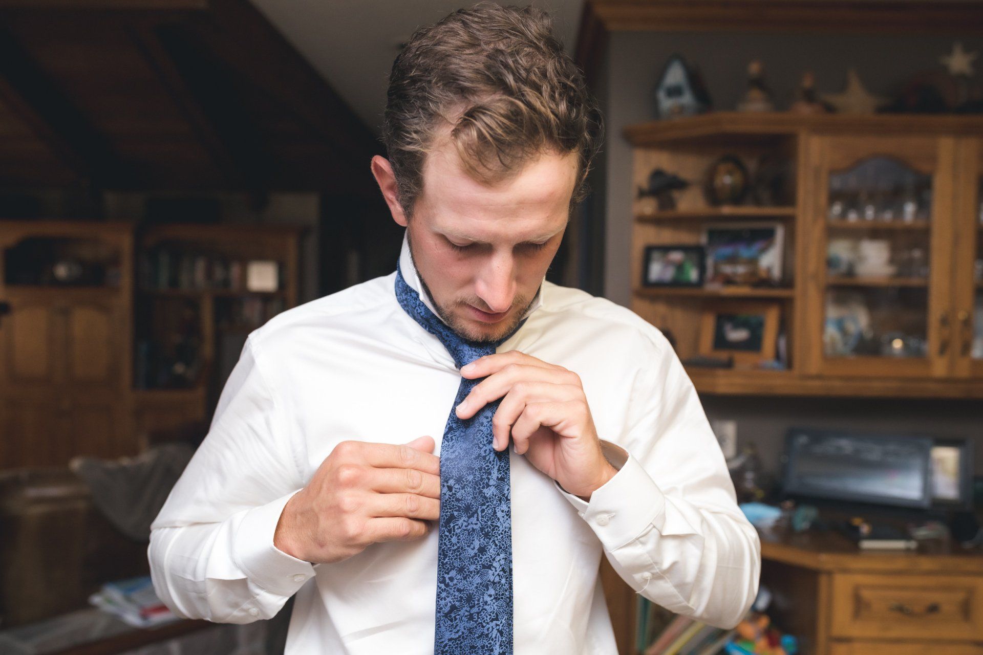 A man is adjusting his tie in a living room.