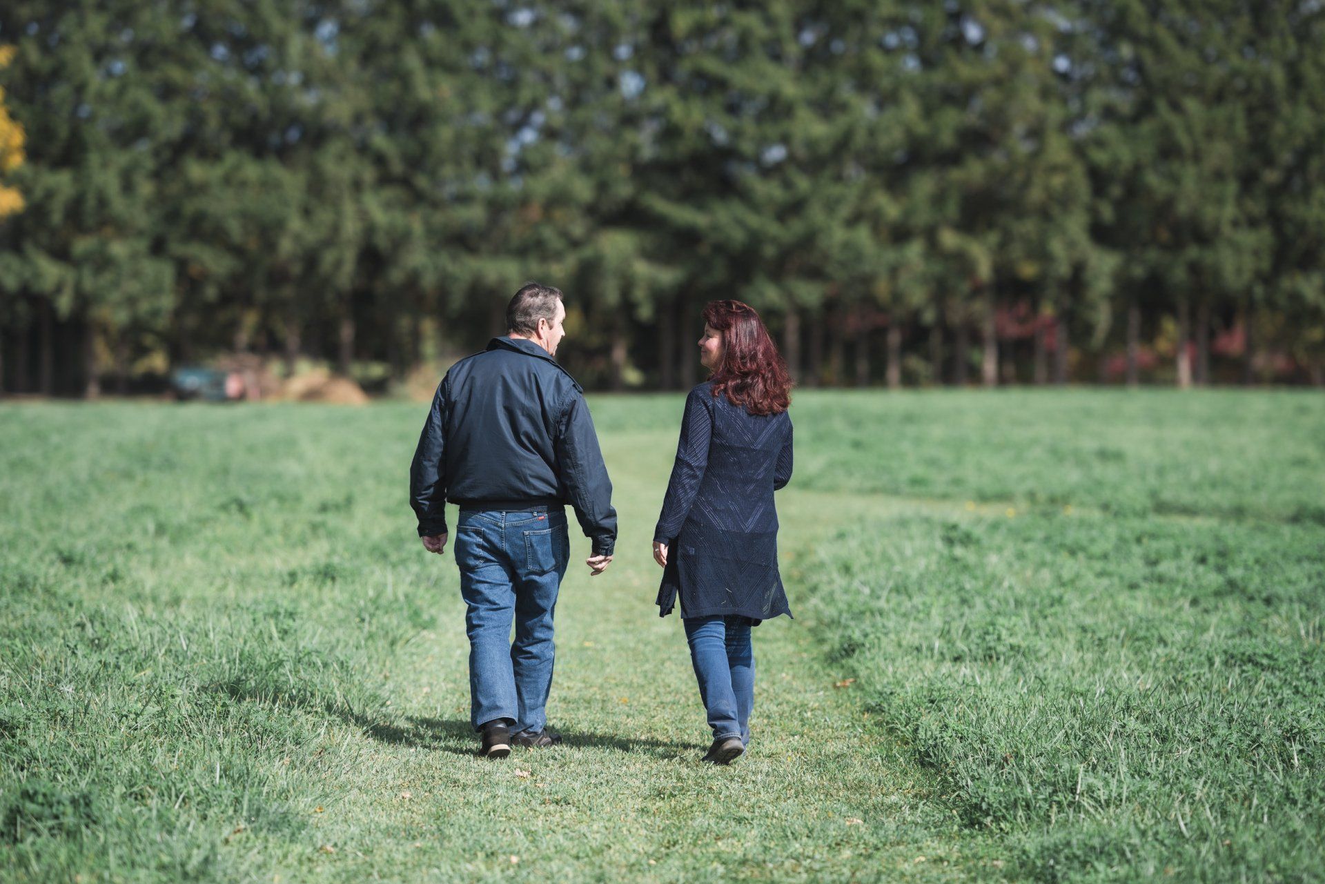 A man and a woman are walking through a grassy field holding hands.