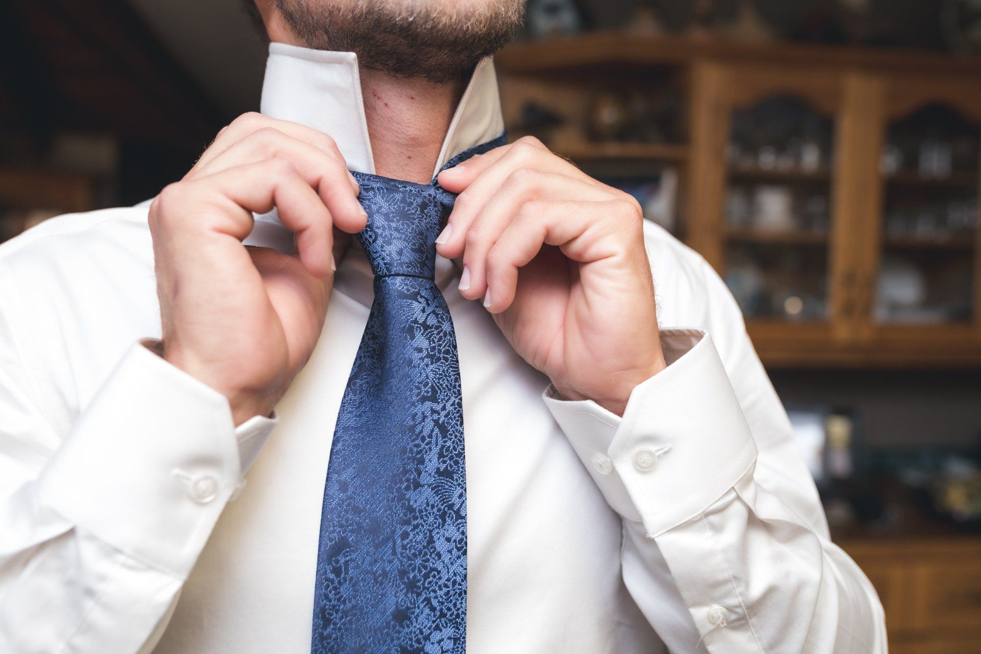 A man in a white shirt is tying a blue tie.