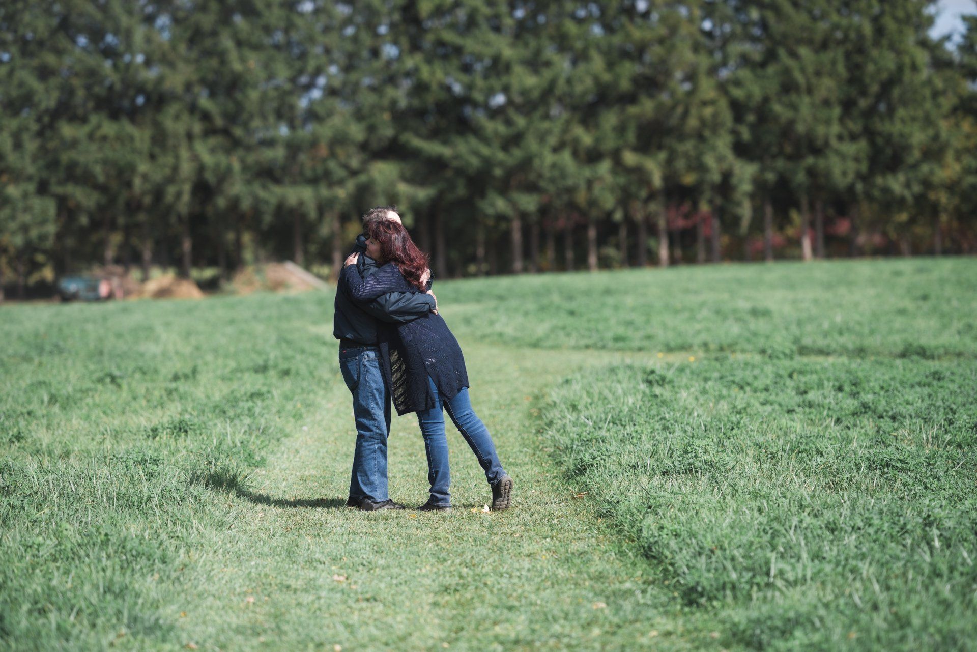 A man and a woman are hugging in a grassy field.