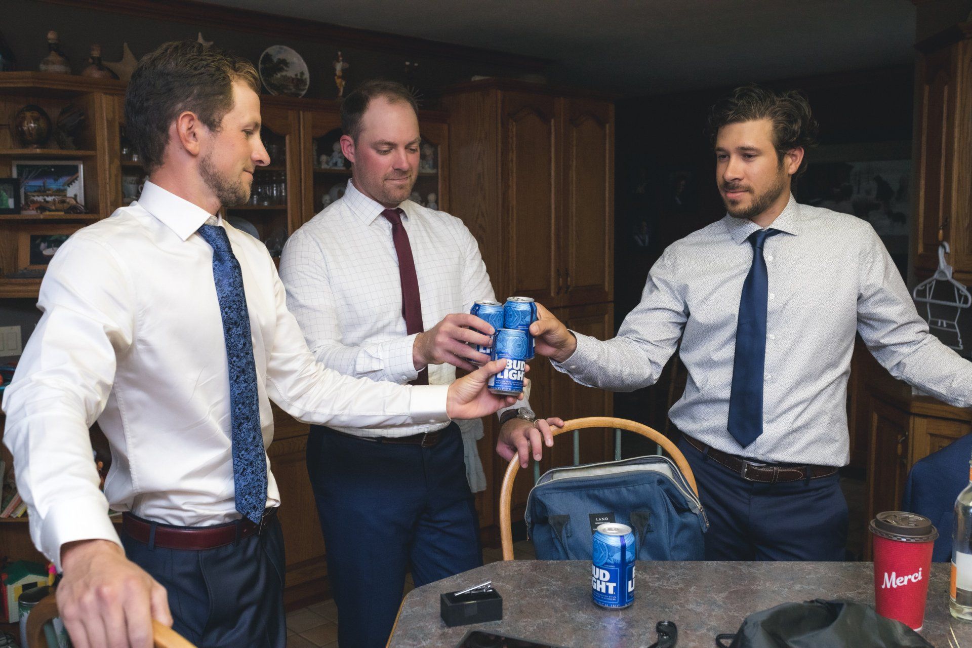 Three men in suits and ties are toasting with cans of soda.