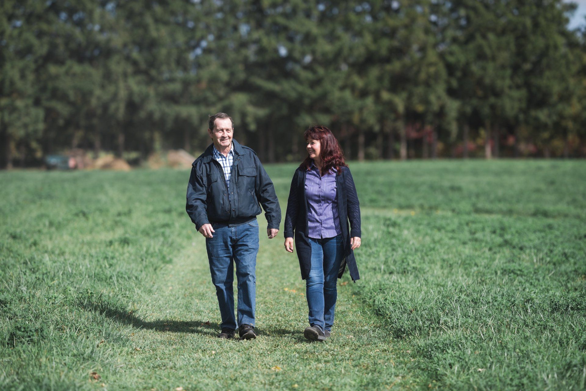 A man and a woman are walking through a grassy field.