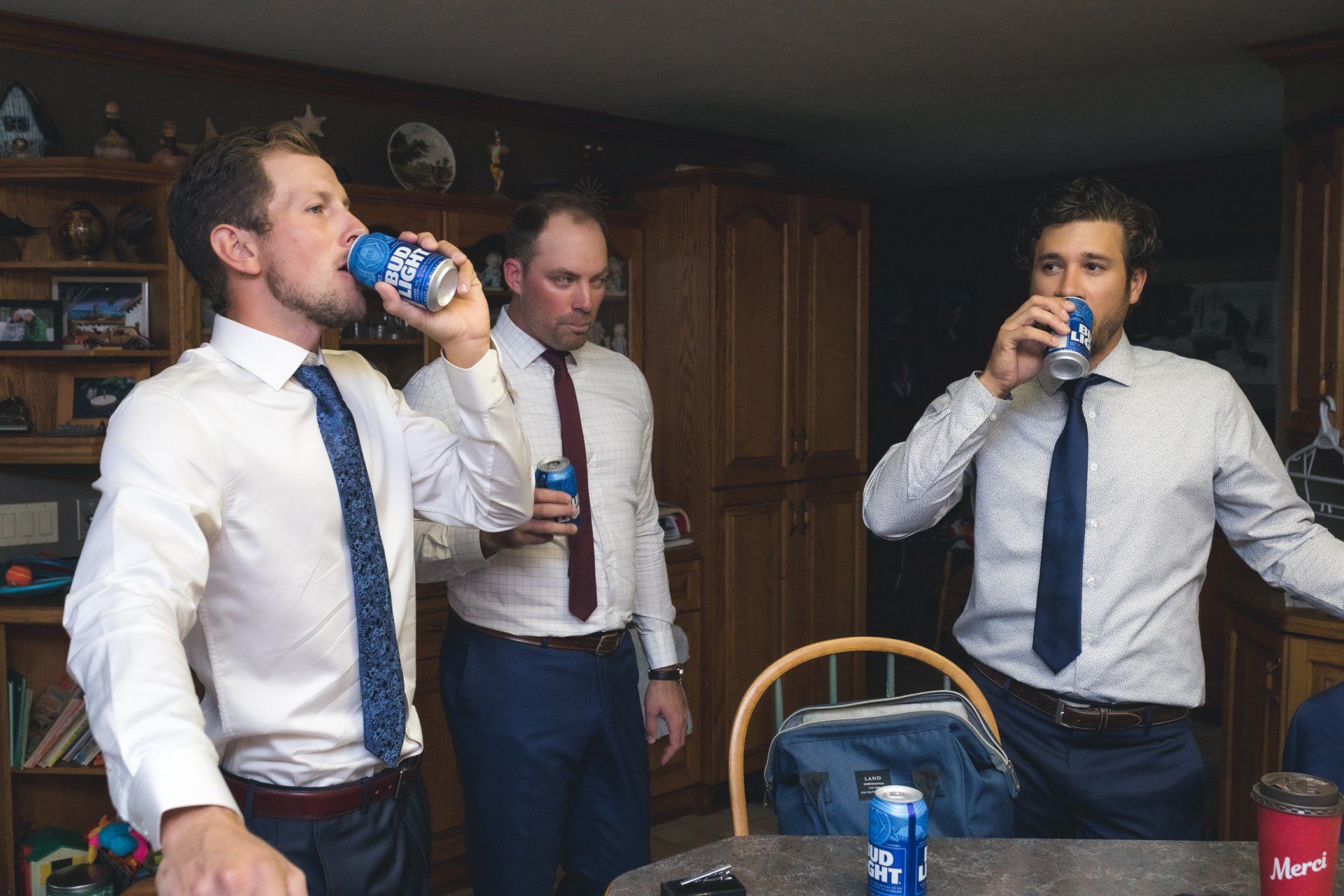 Three men in suits and ties are drinking beer in a living room.