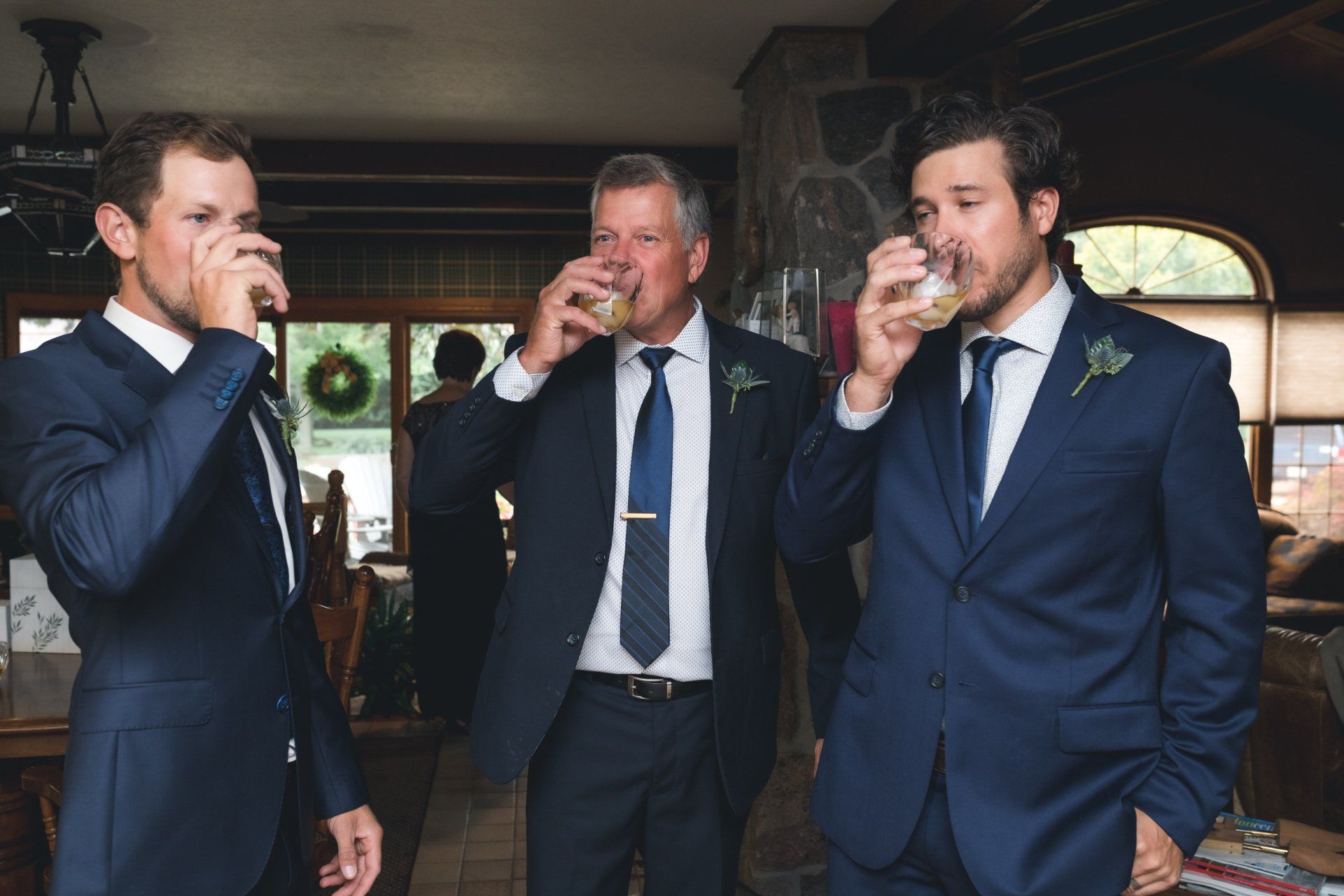 Three men in suits and ties are drinking from glasses in a room.