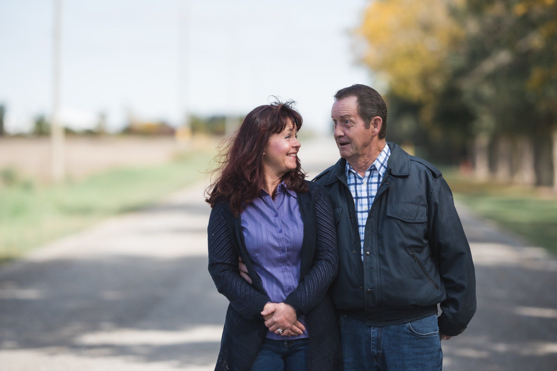 A man and a woman are walking down a road holding hands.