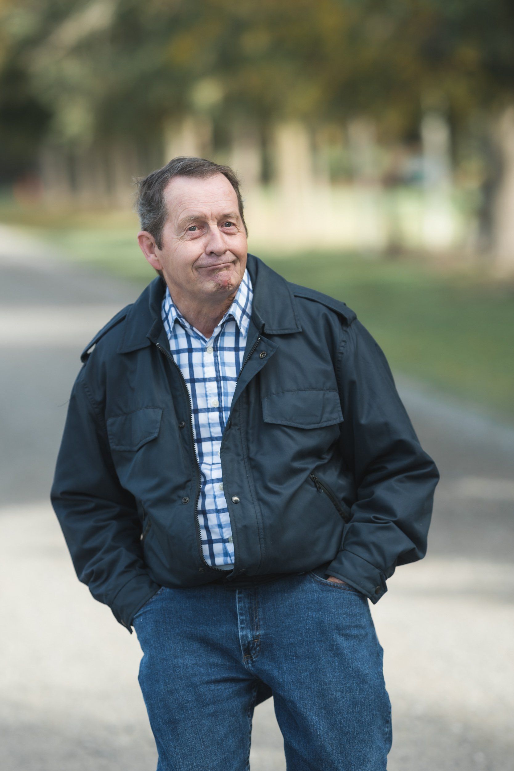 A man in a black jacket and plaid shirt is standing with his hands in his pockets.