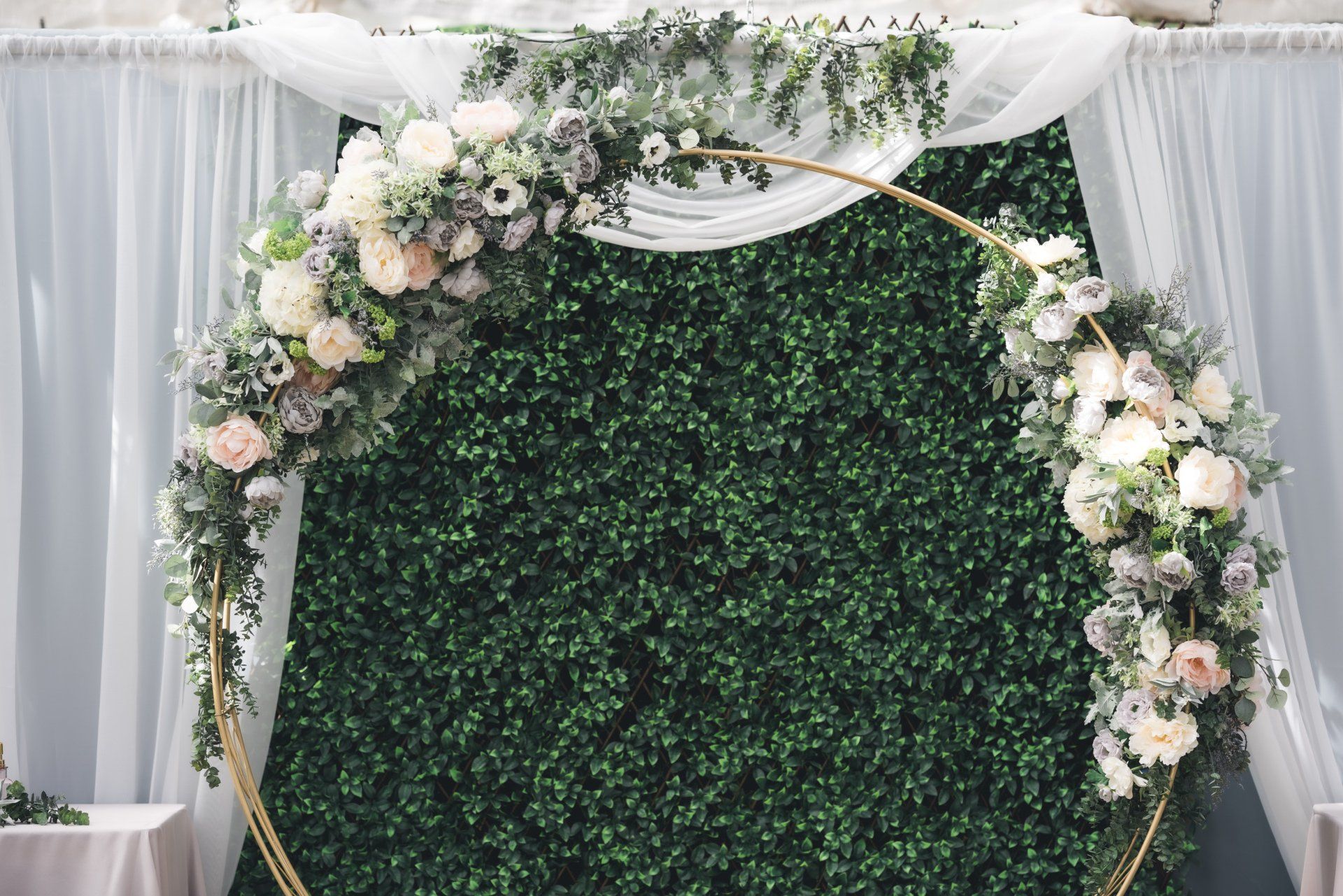 A wedding arch decorated with flowers and greenery is sitting in front of a green wall.