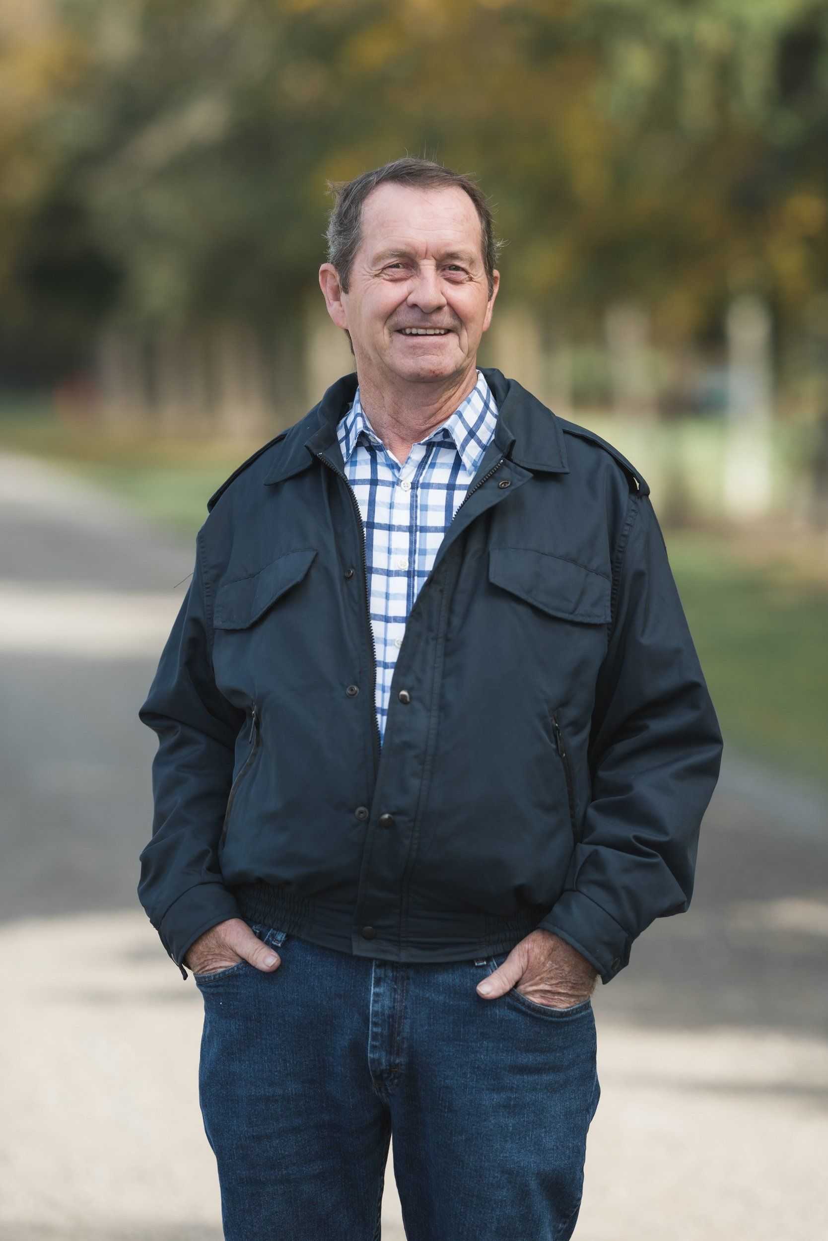 A man in a black jacket and plaid shirt is standing with his hands in his pockets.